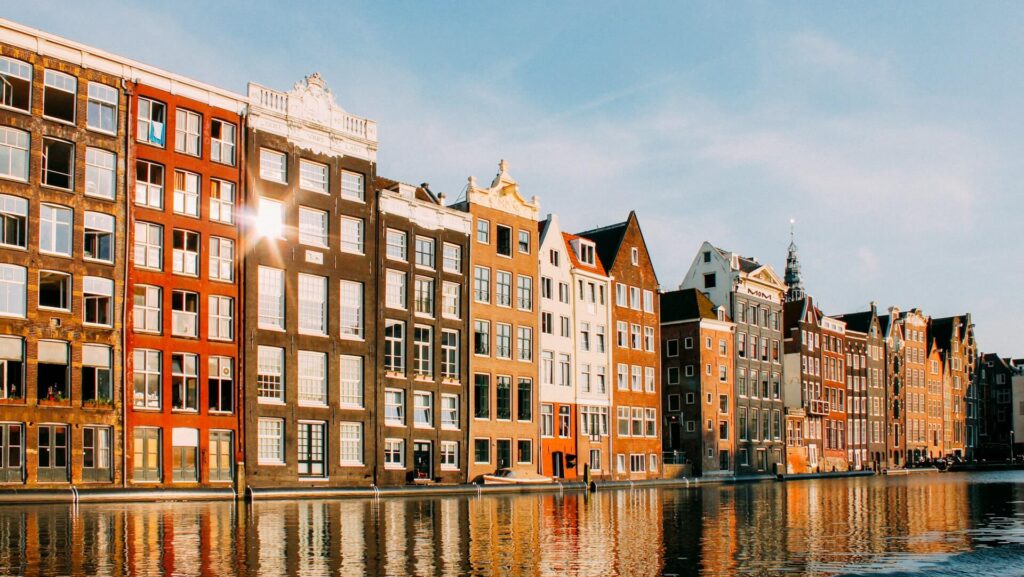 Hoge grachtenpanden in warme avondzon weerspiegelen in het water van een Amsterdamse gracht