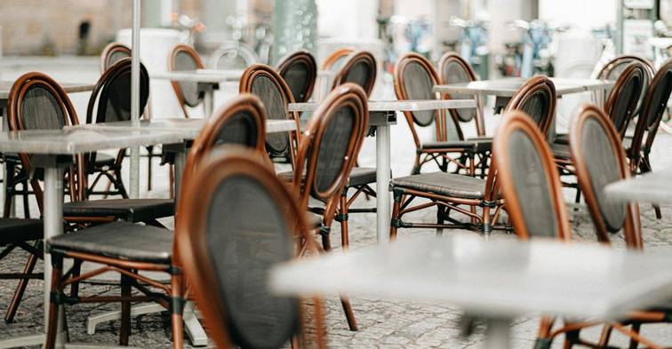 Lege terrastafels en rieten stoelen op een geplaveid plein in een Europese stad