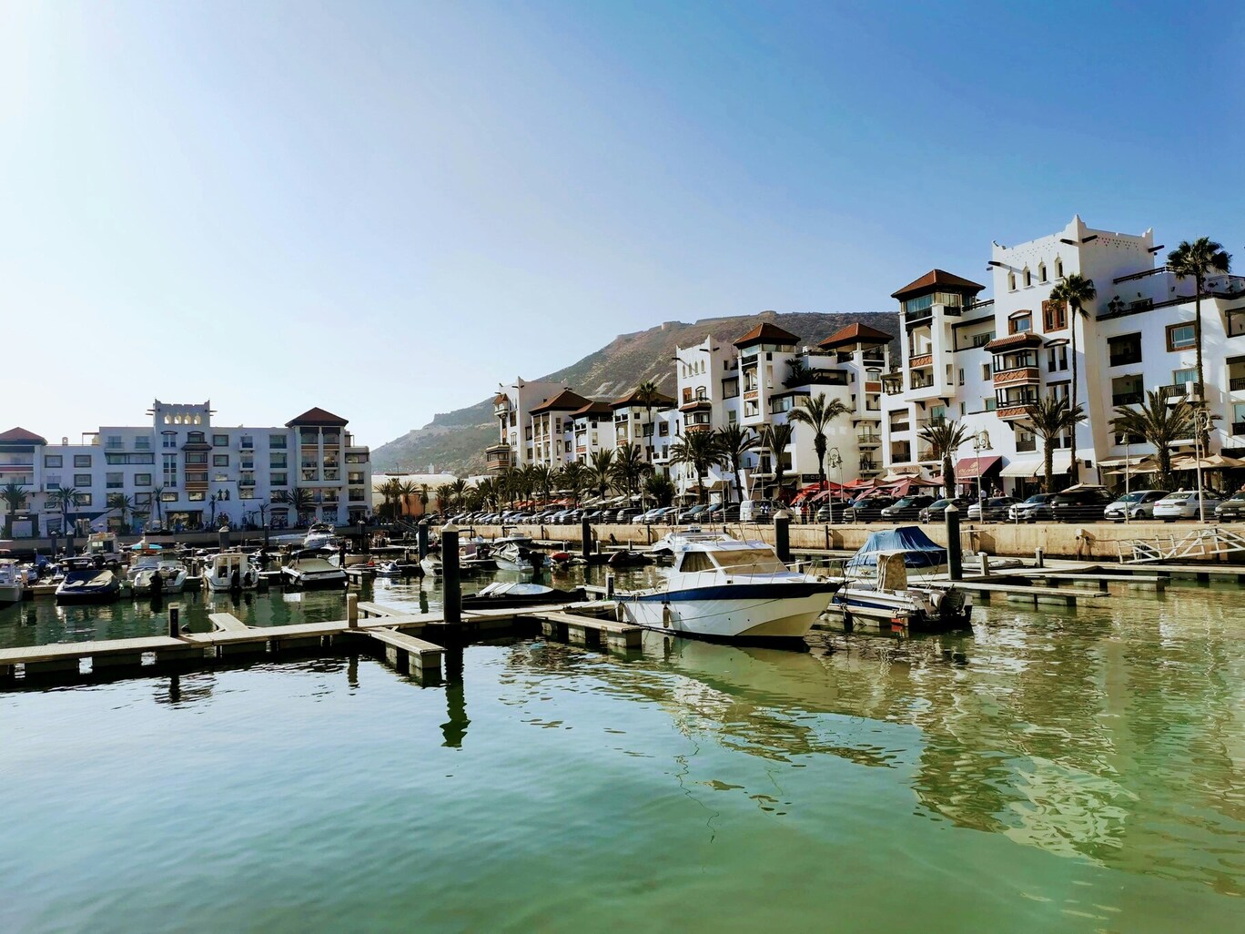 Jachthaven van Agadir met boten, palmbomen en witte gebouwen aan het water.