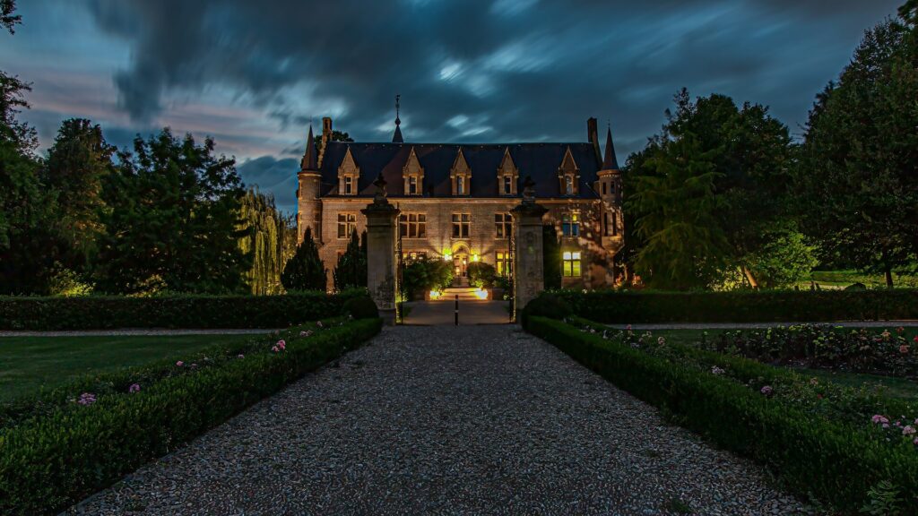 Verlicht kasteel met torentjes achter een oprijlaan van grind, omgeven door tuinen bij schemering, een van de fraaie kastelen bij Heerlen